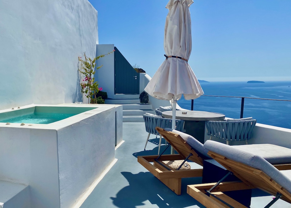 A jacuzzi on a private terrace behind a pair of sunbeds and dining table above the caldera at Ikies hotel in Oia, Santorini.