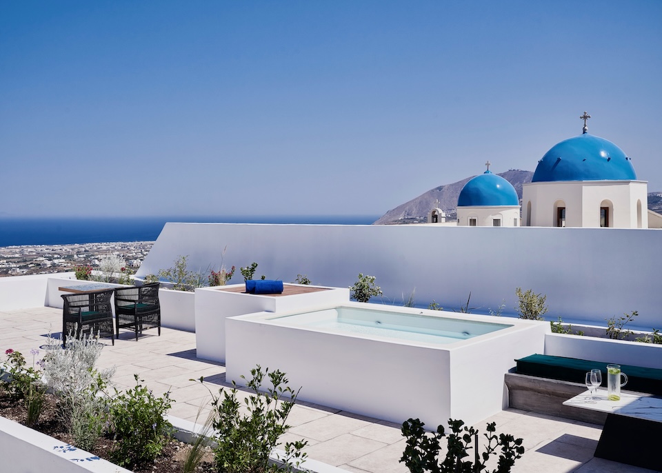 A private plunge pool on a furnished rooftop terrace with a view of two blue church domes and the Aegean Sea at Katikies Garden hotel in Fira, Santorini.