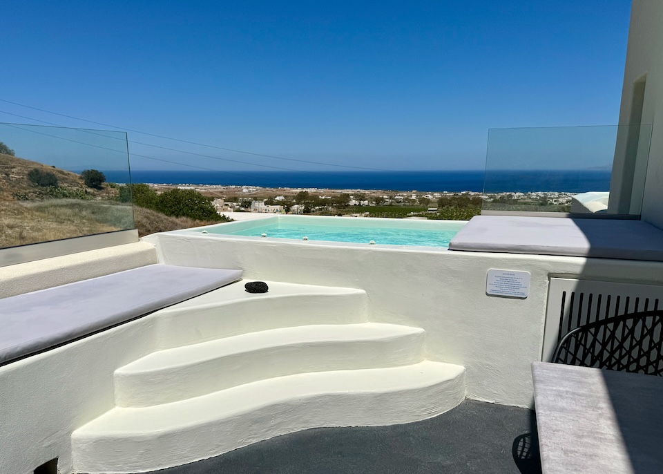 Three steps lead up to an outdoor jacuzzi on a terrace with glass sides and an east-facing view of the sea at Maeva Suites in Episkopi Gonias, Santorini.