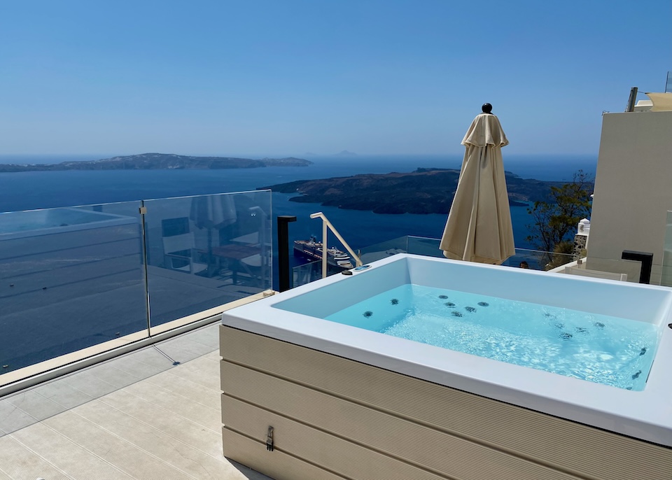 A private jacuzzi on a terrace with glass walls and views to the caldera and volcano at Mythical Blue hotel in Fira, Santorini.