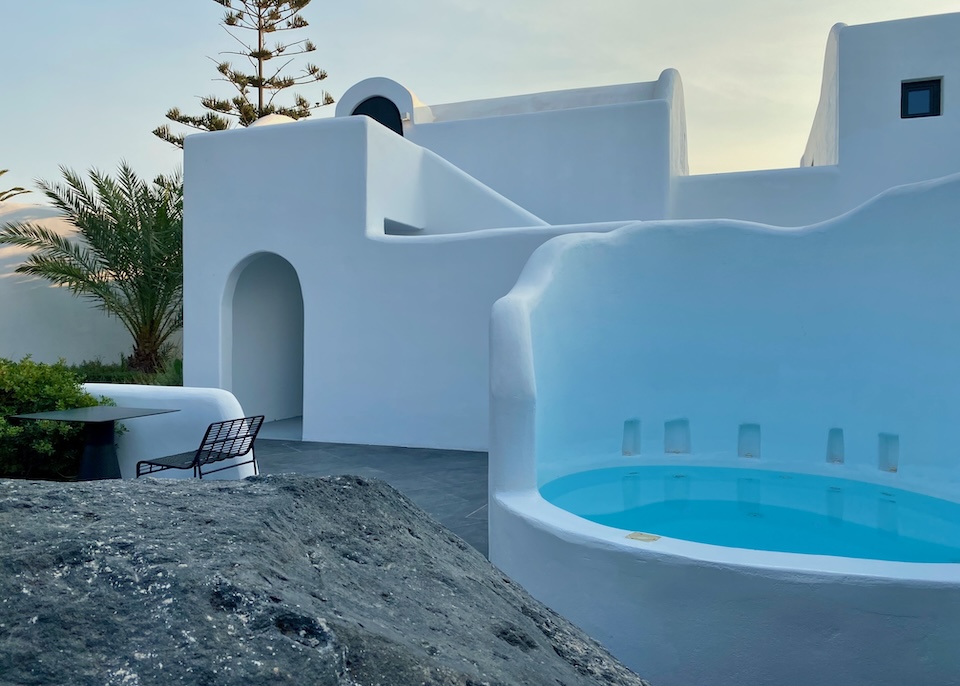 A round plunge pool with a semi-circle high wall and a whitewashed building behind at Nobu hotel in Imerovigli, Santorini.