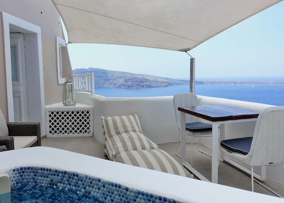 A private jacuzzi, white on top, with round tiles inside on a a furnished, covered terrace overlooking the caldera at Art Maisons Oia Castle hotel in Santorini.