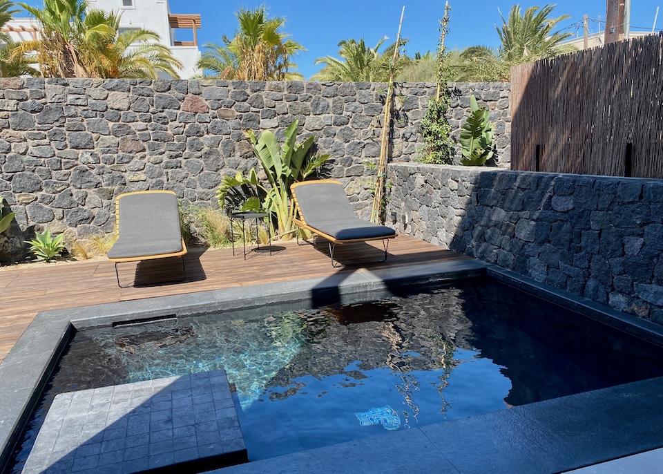 A gray-black sunken private plunge pool on the back patio with sunbeds and lava rock walls at Radisson Blu Zaffron resort in Kamari, Santorini