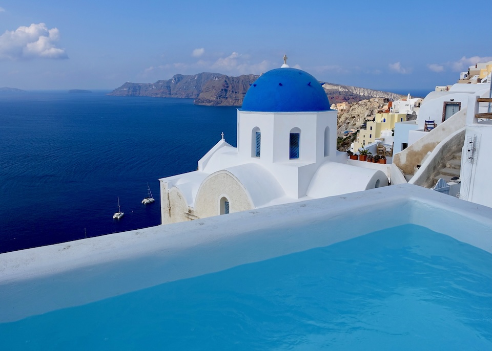 An outdoor private plunge pool facing a blue-domed church and the caldera with catamarans in the water at Sophia Oia View in Santorini