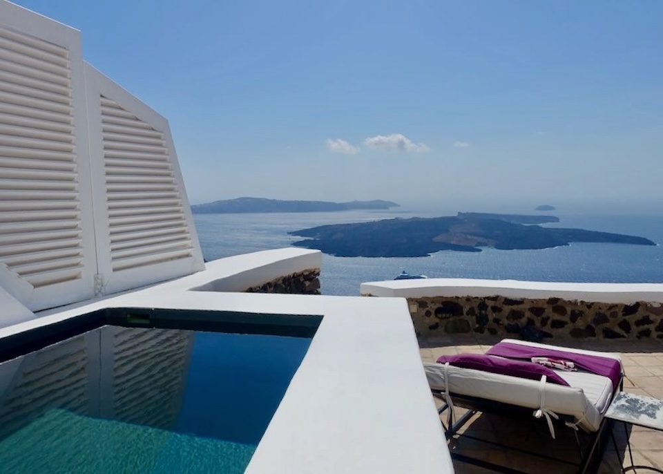 A private plunge pool next to a sunbed with a view over the caldera toward the volcano and Akrotiri Peninsula in Imerovigli, Santorini.