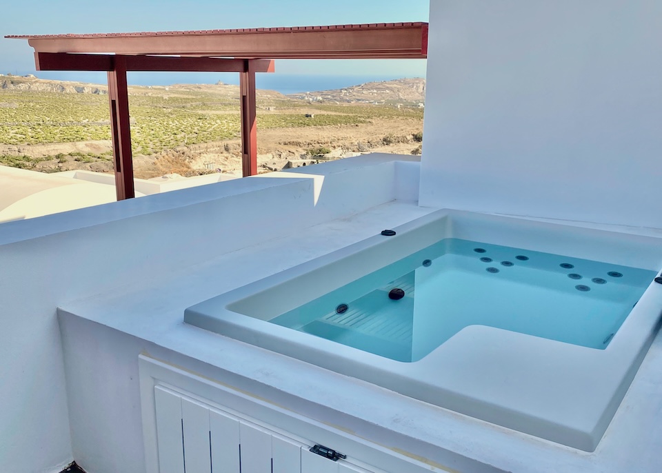 A private jacuzzi on a balcony with views toward vineyards and the sea in the distance at Vedema Resort in Megalochori, Santorini.