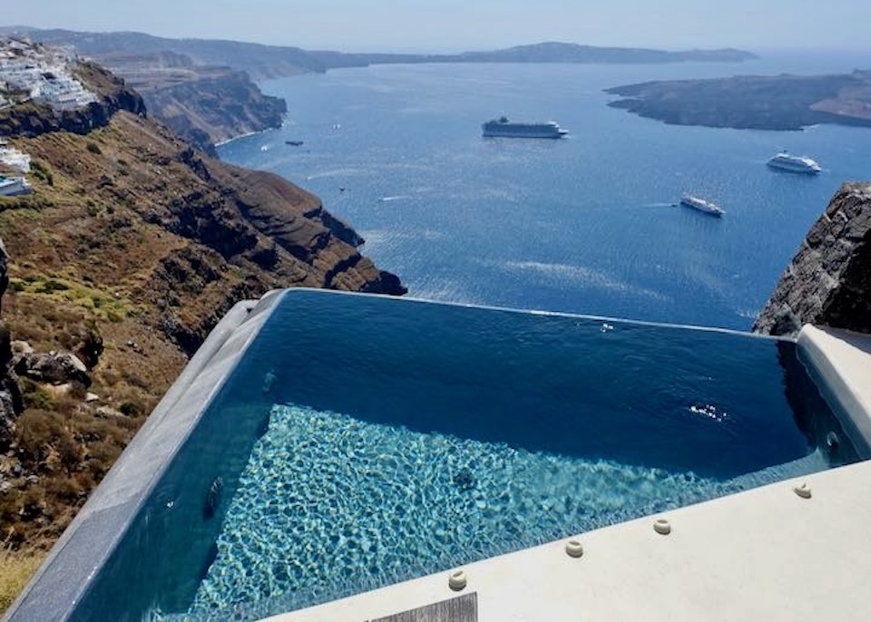 A sharp-angled infinity pool that appears to levitate above the caldera with the volcanoes and cruise ships below at Vora Villas in Imerovigli, Santorini.