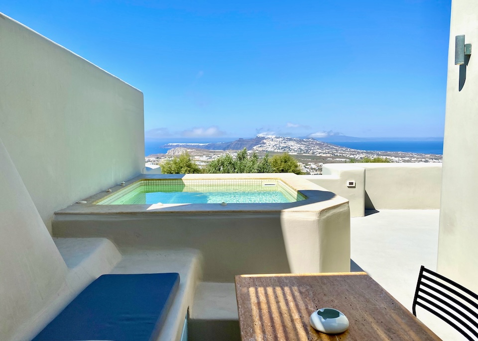 A jacuzzi at the far side of a terrace with a dining space and panoramic views at Voreina Gallery Suites in Imervigli, Santorini.