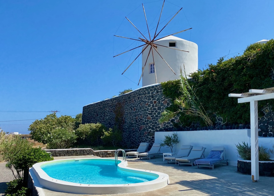 A kidney-shaped private pool on a garden terrace under a windmill at Windmill Villas in Imerovigli, Santorini.