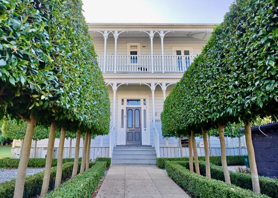 A line of trees follow a path to a front door to a house.