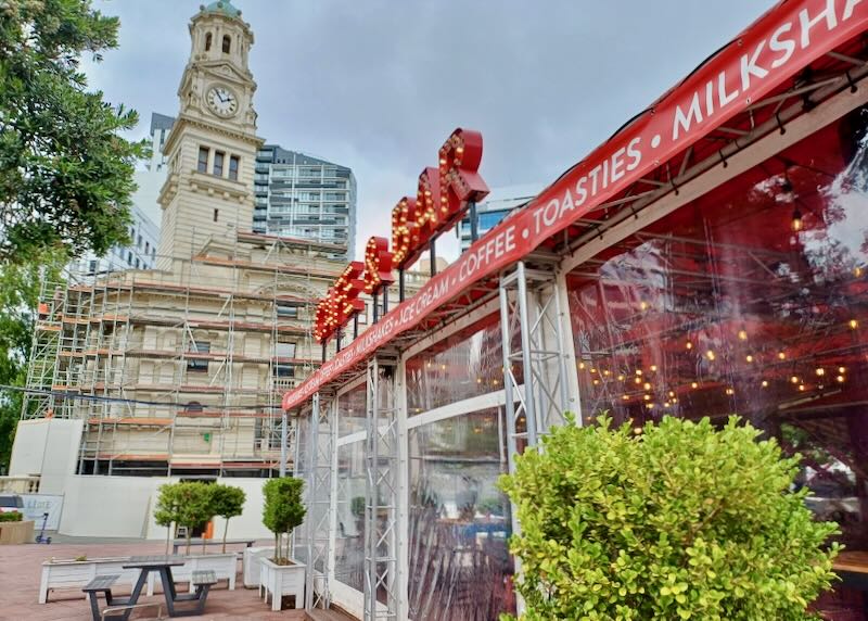 A red sign reads, "Cafe" in a city square.