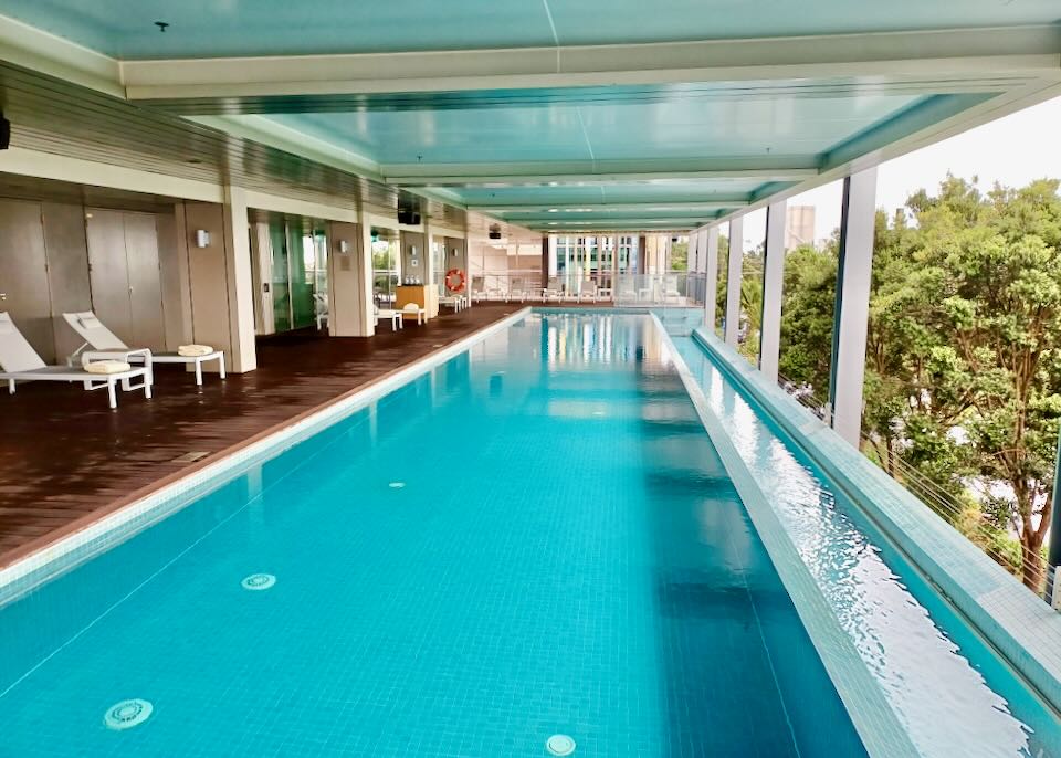 A covered long blue pool surrounded by a wooden deck.