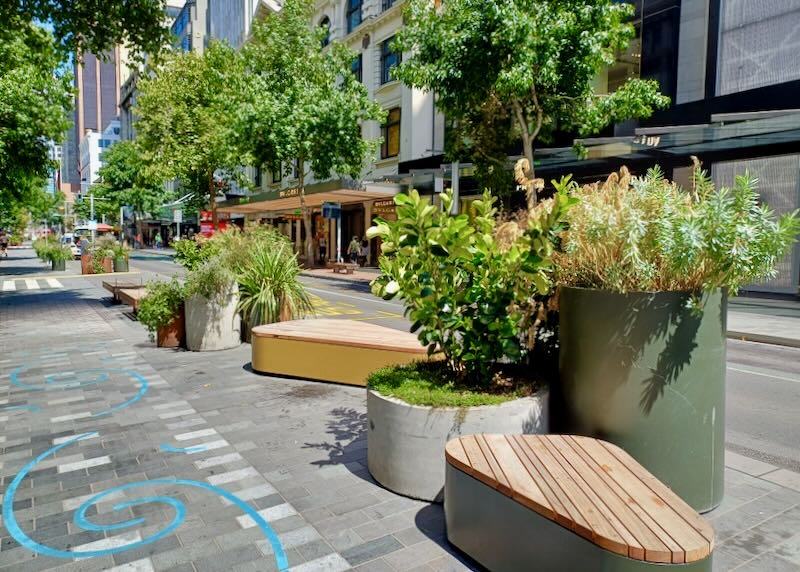 Wood benches and planters sit beside a city street.