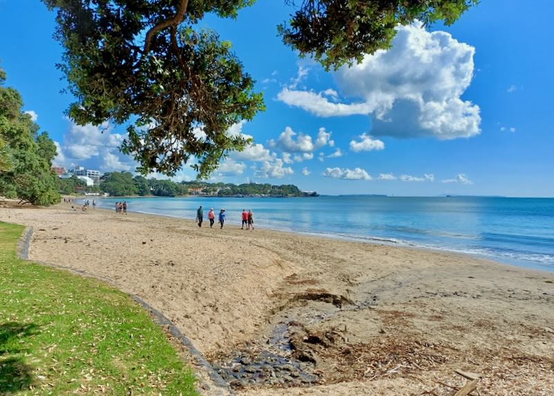 People walk along a beach under puffy clouds.