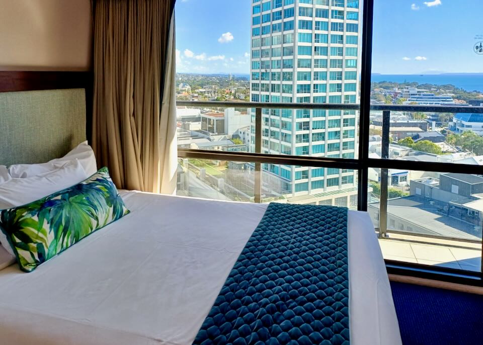 A bed in a hotel sits next to a window with a view of water.