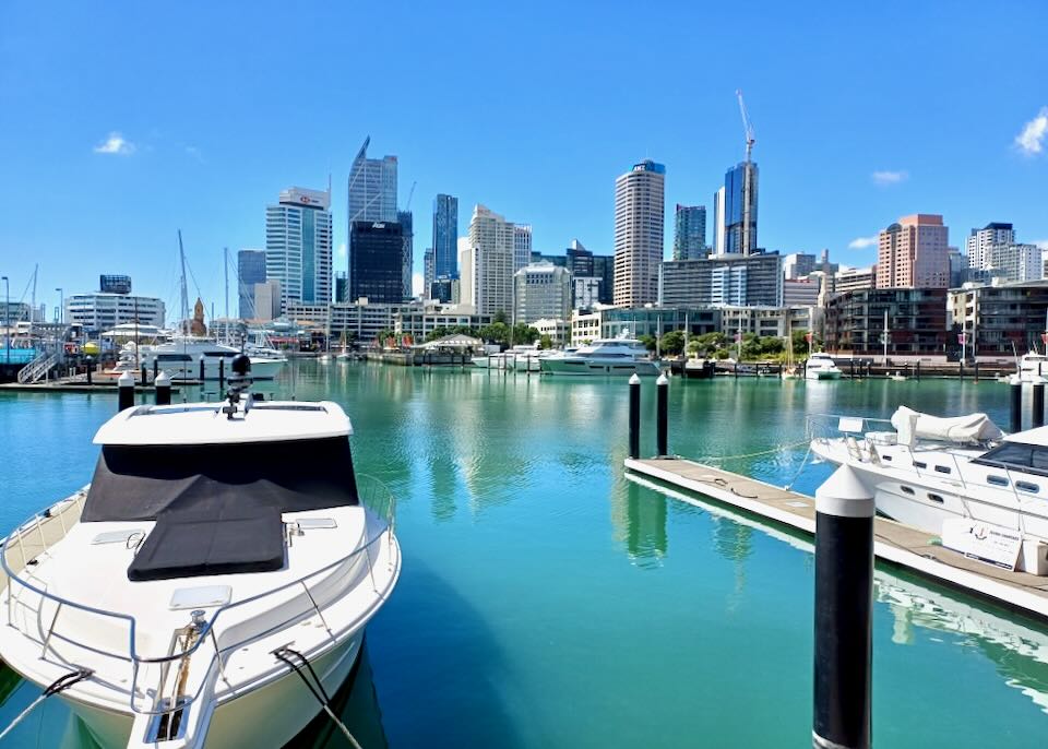 A boat sits in a blue harbor in front of a city skyline.