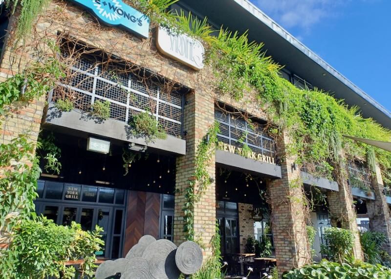 A brink building with small restaurants has green plants hanging on it.