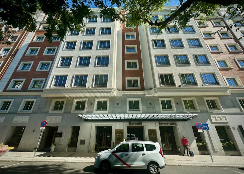 Exterior of a hotel on a tree-lined street, with a small van parked in front.