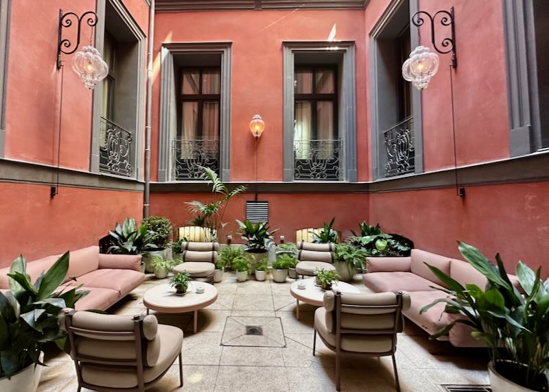 Outdoor courtyard seating area with plush cushioned furnishings, surrounded by red painted walls 