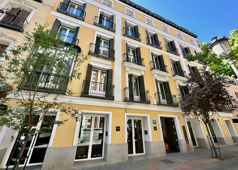 Yellow hotel with black shutters on a tree-lined street in Madrid