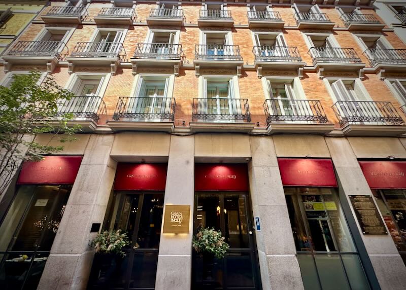 View looking up at a sophisticated brick hotel with red underlit awnings