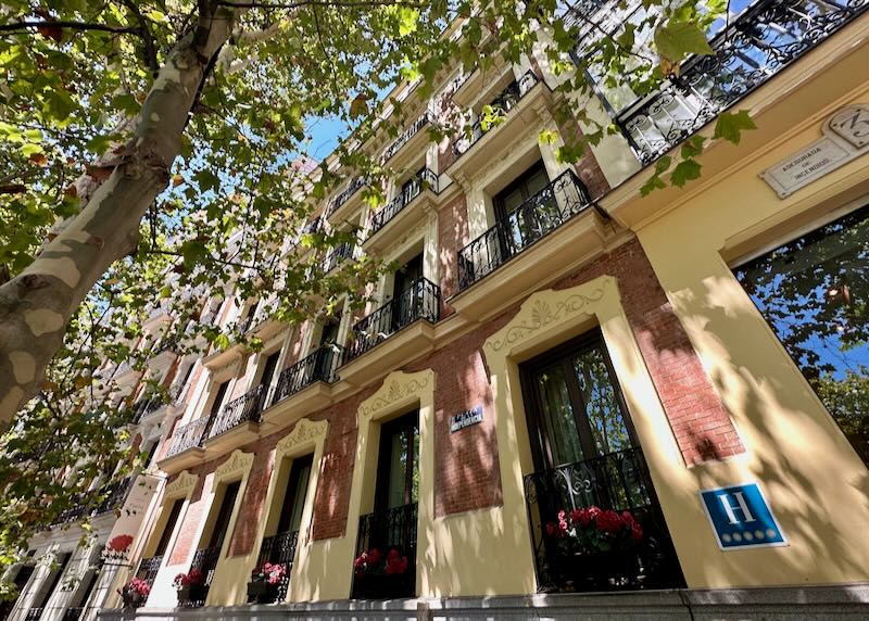 Exterior of a salmon and cream colored hotel on a tree-shaded street