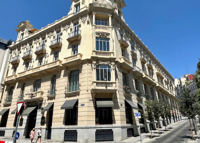 Corner view of a mid-sized cream colored stone hotel with grey awnings