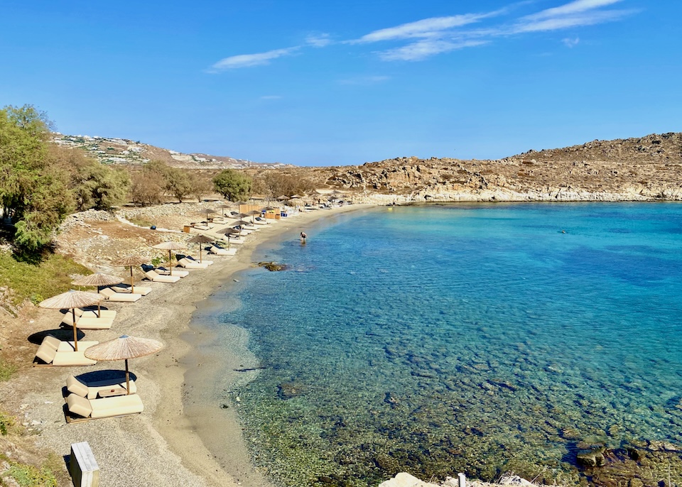 A row of sunbeds and umbrellas with a crystal clear sea at skinny Glyfadi Beach in Aleomandra, Mykonos.