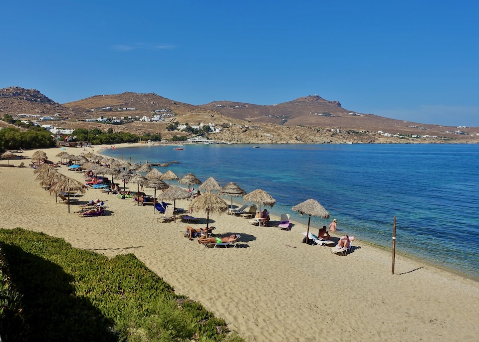 A wide sandy beach with three rows of sunbeds and thatched umbrellas on Kalafatis Beach in Mykonos.