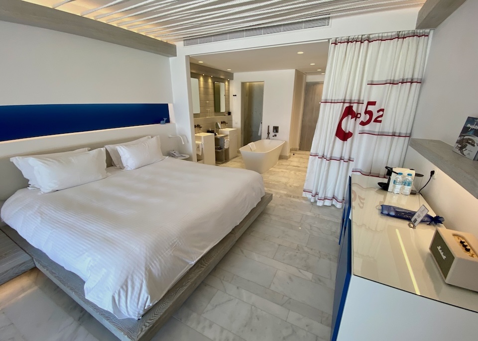 A king-sized bed in white set in a nautically inspired room with a freestanding soaking tub at Mykonos Riviera in Tourlos.