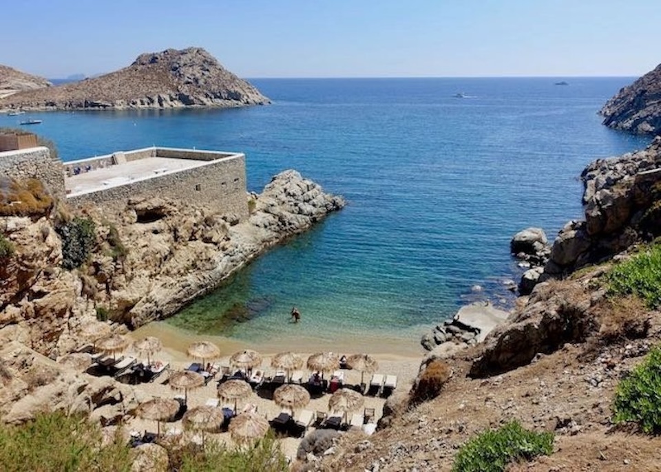 Three rows of sunbeds and thatched umbrellas tucked away in a a small private beach at The Wild Hotel by Interni near Kalafati, Mykonos.