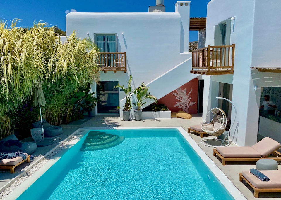 A rectangular pool in the courtyard of a whitewashed hotel, partially shaded by bamboo, at Adorno Beach Hotel in Ornos, Mykonos.