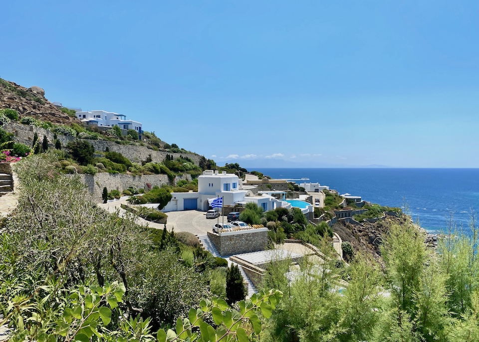 A large villa with a pool and stone walls is nestled in greenery above the sea at AGL Luxury Villas in Agios Lazaros, Mykonos.