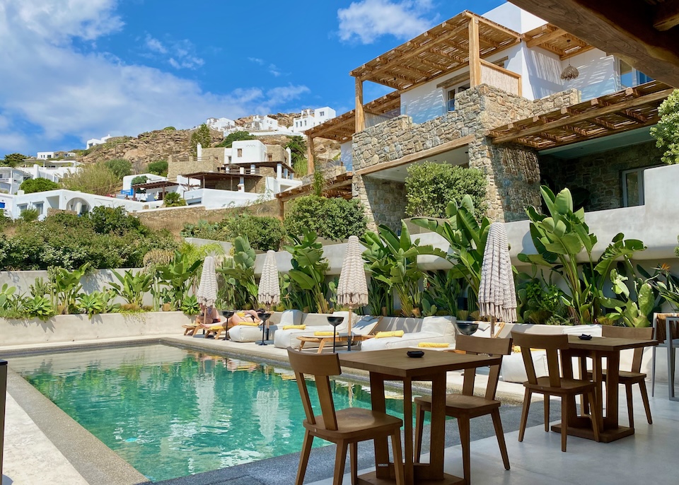 A swimming pool in a garden setting with a row of sunbeds and hotel balconies rising in the background at Amyth of Mykonos in Agios Stefanos, Mykonos.