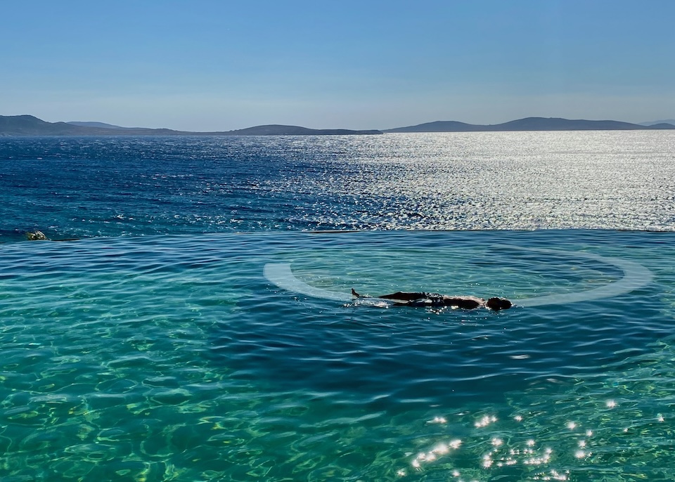 A man laying face up in an infinity pool that seems to blend into the sea at Anax Resort in Agios Ioannis, Mykonos.