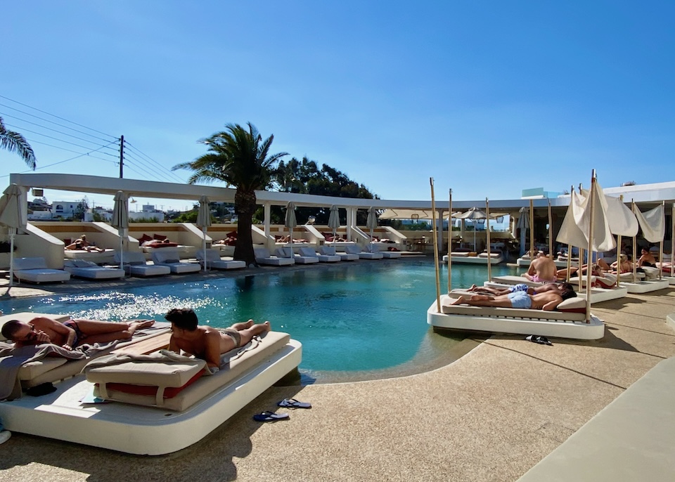 A freeform pool encircled by sunbeds, umbrellas, and sail cloths at Andronikos Hotel in Drafaki, Mykonos.