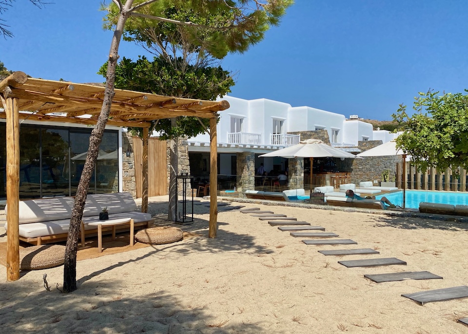 A wooden pathway through the beach passing by a pool and cabana at Bill and Coo Coast Suites in Agios Ioannis, Mykonos.