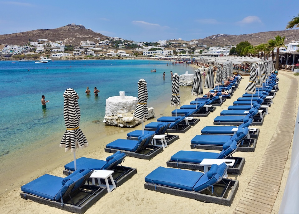 Two rows of sunbeds line the beach in the foregroudn with beach clubs stretching out into the distance at Mykonos Blanc hotel in Ornos, Mykonos.