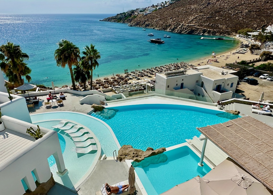 View from above three different shapes and sizes of pools overlooking a beach and sea at Mykonos Blu resort in Psrrou, Mykonos.