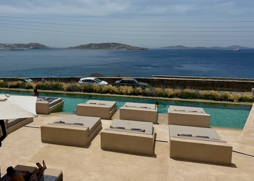 Two rows of double-sized sunbeds sit behing a pool facing the sea at Domes Noruz hotel in Agios Stefanos, Mykonos.