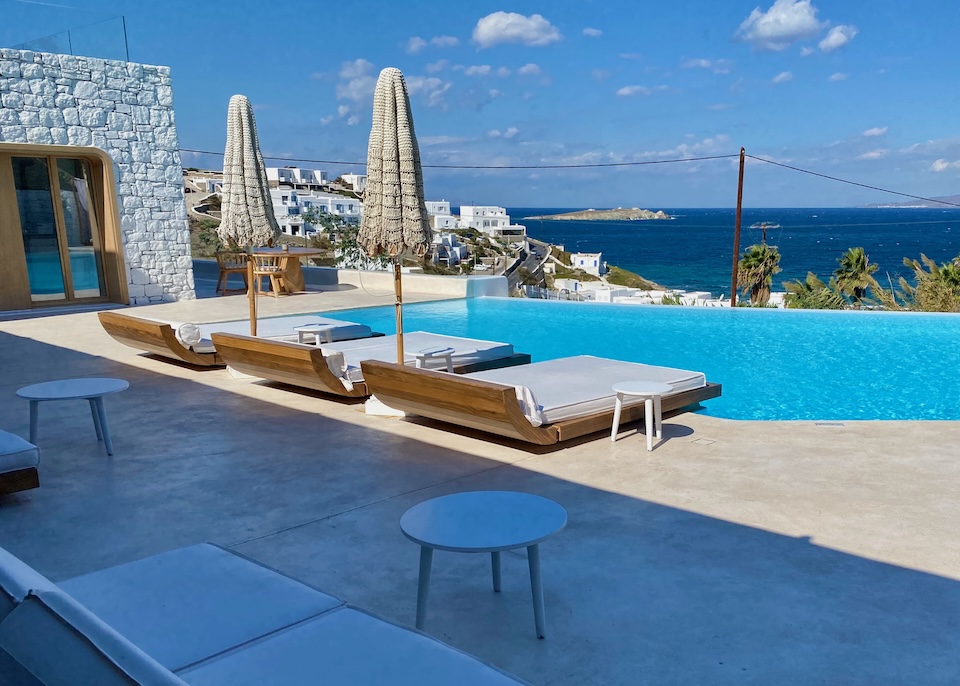 An infinity pool facing the sea with three double-sized sunbeds on the near side at Mykonos Earth Suites in Megali Ammos, Mykonos.