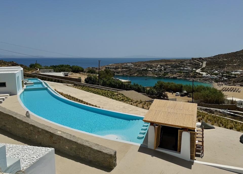 A curved pool with a swim up bar at one end and private, sectioned off mini pools at the other end at Mykonos Flow above Super Paradise Beach.