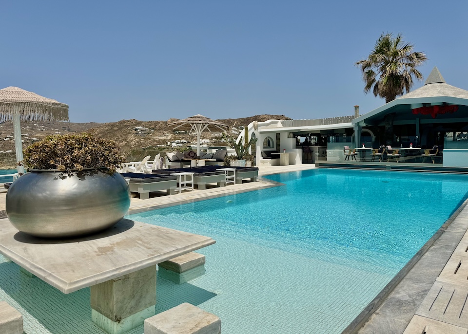 An infinity pool with sunbeds one one side and a pool bar at the far end at Greco Philia hotel in Elia, Mykonos.