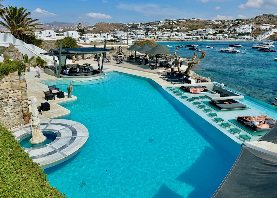 An infinity pool with a glassed-in section of sunbeds, swim up bar, and restaurant facing the sea at Kivotos hotel in Ornos, Mykonos.