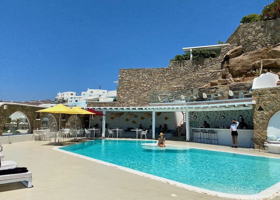 A swimming pool in front of a natural stone building that blends into the hillside at Kouros Hotel on the edge of Mykonos Town.