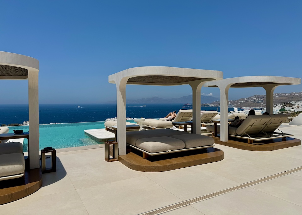 Contemporary cabanas with plush sunbeds sit behind an infinity pool above the sea at Lovia hotel on the hills above Mykonos Town.