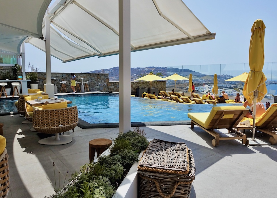 An infinity pool sits behind a few rows of sunbeds above the sea at Myconian Korali above Megali Ammos Beach in Mykonos.