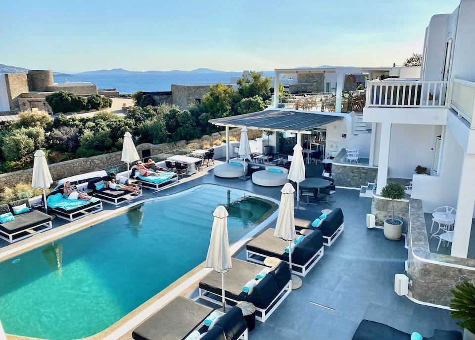 View looking down toward an infinity pool with sunbeds all around it and a pool bar at Mykonos Princess hotel in Agios Stefanos, Mykonos.