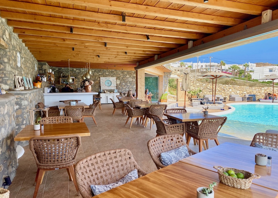 A poolside restaurant and bar with a terra cotta floor, stone walls, and a wooden roof at Salty Houses near Kalo Livadi in Mykonos.