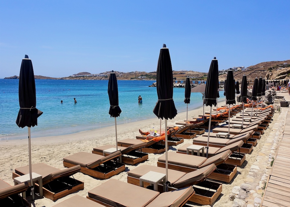 Two rows of sunbeds and umbrellas stretch far across the sand on a calm beach at Santa Marina resort in Ornos, Mykonos.